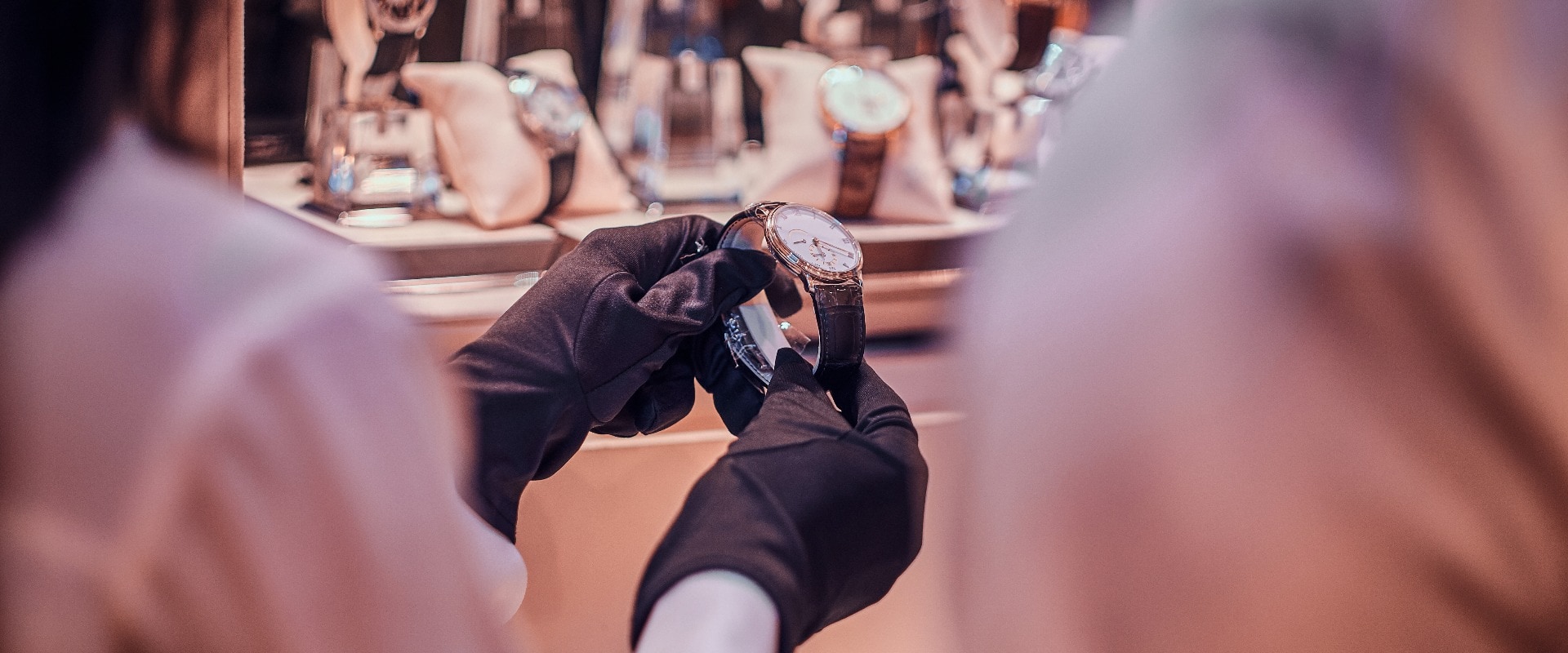 Verkäuferin mit schwarzen Handschuhen zeigt teure Uhr für einen Kunden