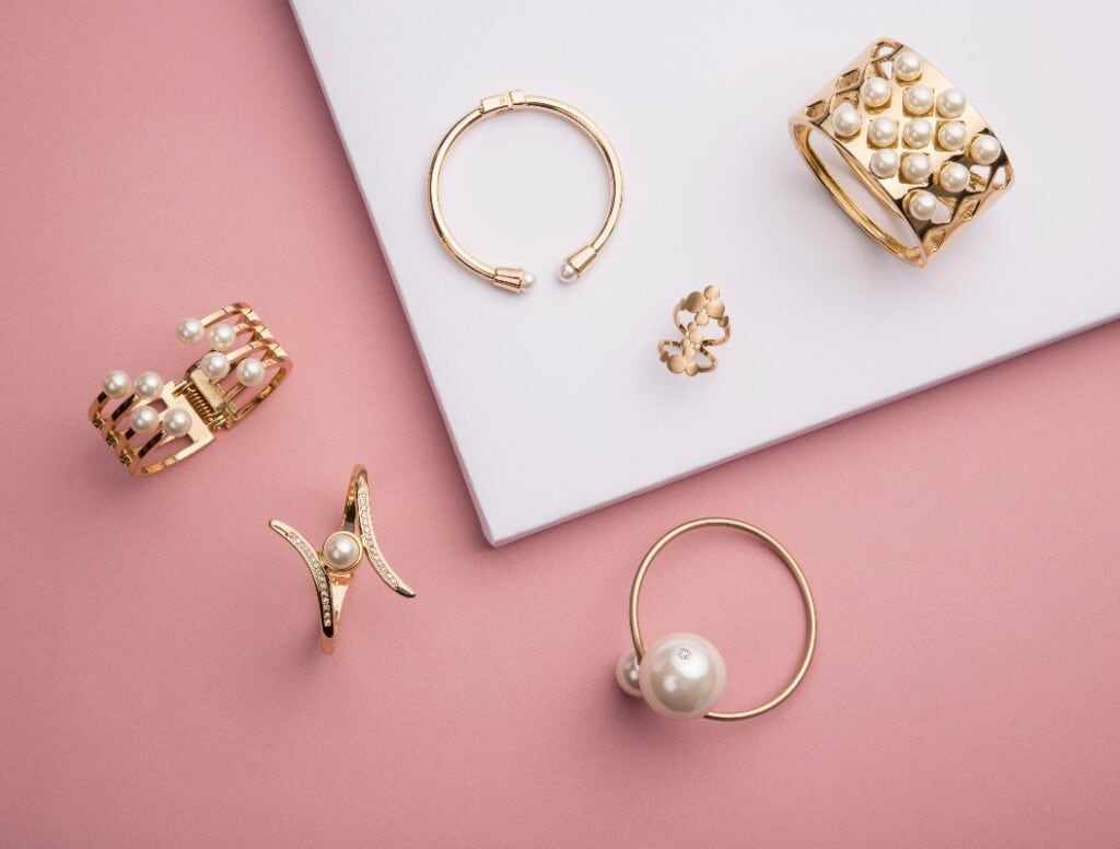 Perle Goldene Armbänder und Ring auf rosa und weißem Hintergrund